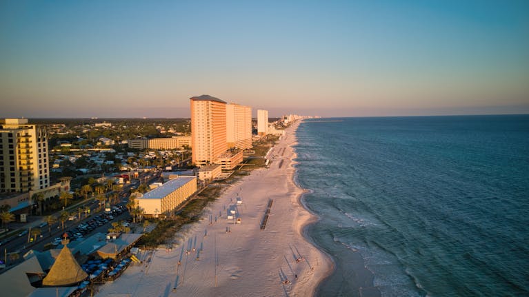 A stunning aerial view of a coastal city with tall buildings and a beautiful beach at sunset.